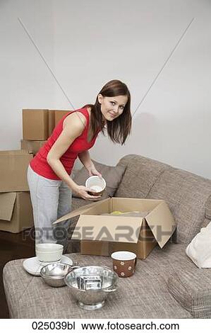 Stock Image - young woman packing crockery in moving box. Fotosearch