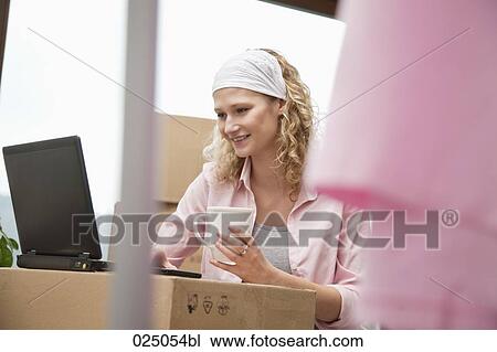 Stock Image - young woman with laptop computer in new home. Fotosearch