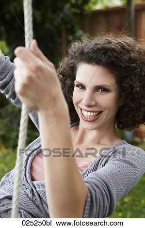 Stock Image - portrait of young woman in garden on swing. Fotosearch