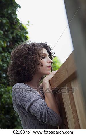 Stock Image - portrait of young woman looking over garden fence. Fotosearch