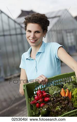 Stock Image - portrait of young woman with basket full of vegetables. Fotosearch