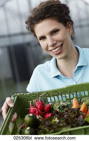 Stock Image - portrait of young woman with basket full of vegetables. Fotosearch