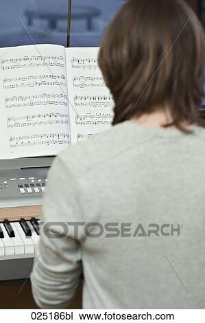 Stock Image - rear view of young woman playing keyboard. Fotosearch