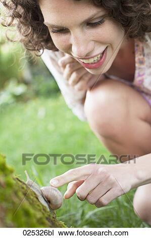 Stock Image - young woman in garden watching snail. Fotosearch