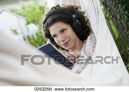 Stock Image - young woman in hammock in garden with earphones and tablet computer. Fotosearch