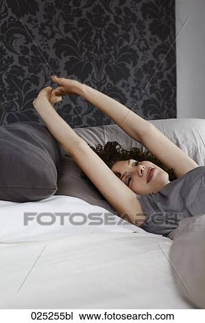 Stock Image - young woman lying in bed stretching. Fotosearch