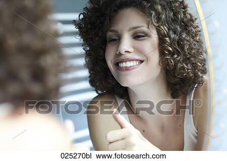 Stock Image - young woman smiling at her reflection in the mirror. Fotosearch