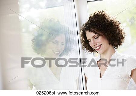 Stock Image - young woman standing by the window. Fotosearch