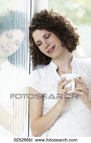 young woman standing by the window with cup of coffee View Large Photo Image Stock Image - young woman standing by the window with cup of coffee. Fotosearch