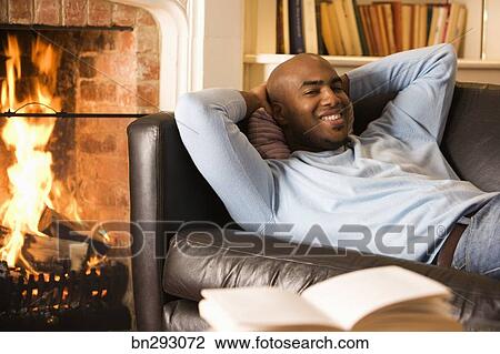 Man Lounging On Sofa Next To Fireplace Stock Image Bn293072
