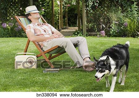 Stock Photo of Man relaxing in lawn chair with dog bn338094 - Search