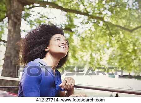 Picture - Carefree woman with afro riding double decker bus and looking up. Fotosearch