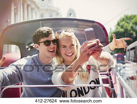 Picture - Couple taking selfie on double-decker bus in London. Fotosearch