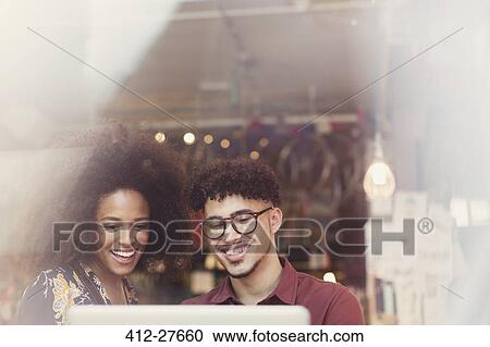 Stock Image - Couple using laptop in cafe window. Fotosearch