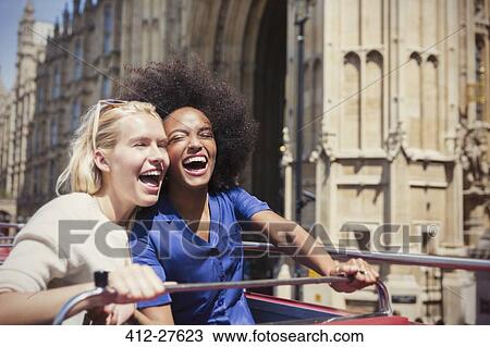 Stock Image - Enthusiastic friends laughing on double-decker bus in London. Fotosearch