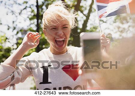 Stock Image - Enthusiastic woman waving British flag being photographed. Fotosearch