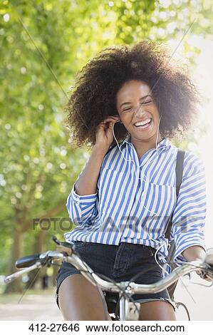 Enthusiastic woman with afro riding bicycle listening to music on headphones View Large Photo Image Stock Photograph - Enthusiastic woman with afro riding bicycle listening to music on headphones. Fotosearch