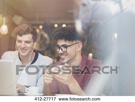 Stock Photo - Friends drinking coffee and using laptop in cafe. Fotosearch