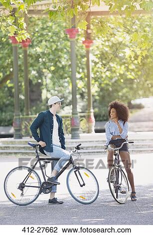 Stock Image - Friends on bicycles talking in urban park. Fotosearch