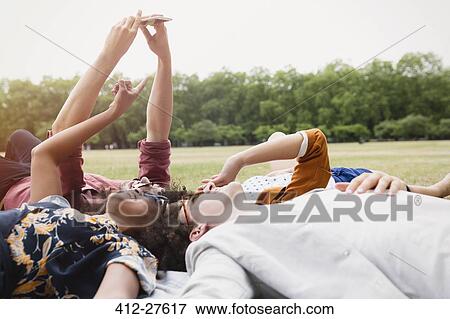 Stock Photo - Friends taking selfie laying in circle in grass. Fotosearch