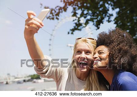 Stock Photograph - Friends taking selfie with London Eye in background, London, United Kingdom. Fotosearch