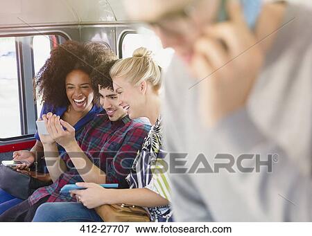 Stock Photo - Friends texting with cell phone on bus. Fotosearch
