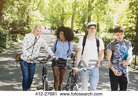 Stock Image - Friends walking with bicycles in park. Fotosearch