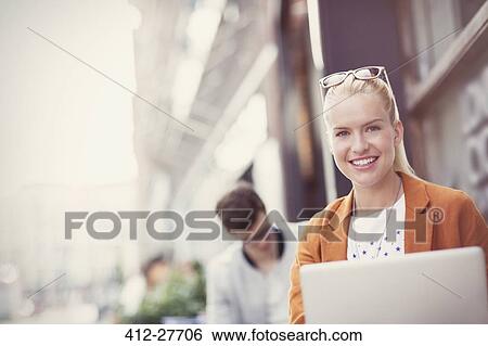 Stock Photograph - Portrait smiling blonde woman with laptop at sidewalk cafe. Fotosearch