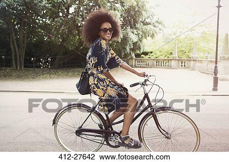Portrait smiling woman with afro riding bicycle in urban park View Large Photo Image Stock Image - Portrait smiling woman with afro riding bicycle in urban park. Fotosearch