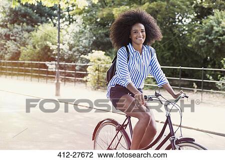 Portrait smiling woman with afro riding bicycle in park View Large Photo Image Stock Image - Portrait smiling woman with afro riding bicycle in park. Fotosearch