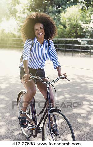 Portrait smiling woman with afro riding bicycle in park View Large Photo Image Stock Photo - Portrait smiling woman with afro riding bicycle in park. Fotosearch