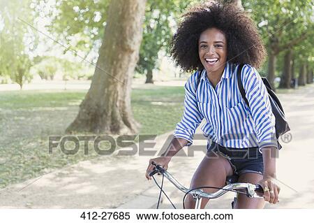 Portrait smiling woman with afro riding bicycle in park View Large Photo Image Stock Photography - Portrait smiling woman with afro riding bicycle in park. Fotosearch
