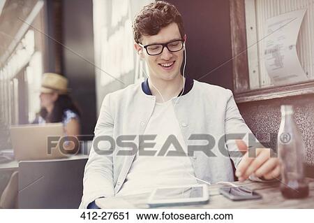 Smiling young man listening to music with headphones and mp3 player at sidewalk cafe View Large Photo Image Stock Image - Smiling young man listening to music with headphones and mp3 player at sidewalk cafe. Fotosearch