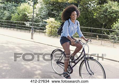 Woman with afro riding bicycle in park View Large Photo Image Picture - Woman with afro riding bicycle in park. Fotosearch