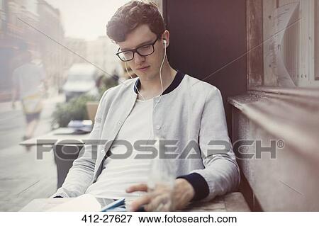 Young man with eyeglasses and headphones using digital tablet at sidewalk cafe View Large Photo Image Stock Photo - Young man with eyeglasses and headphones using digital tablet at sidewalk cafe. Fotosearch