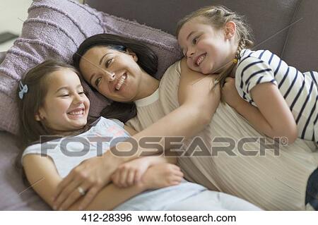 Affectionate mother and daughters cuddling on sofa View Large Photo Image Stock Photograph - Affectionate mother and daughters cuddling on sofa. Fotosearch