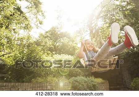 Stock Photo - Carefree girl swinging in sunny backyard. Fotosearch