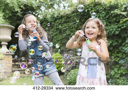 Carefree girls blowing bubbles in backyard View Large Photo Image Picture - Carefree girls blowing bubbles in backyard. Fotosearch