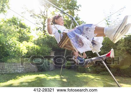 Stock Image - Carefree girls swinging in backyard. Fotosearch