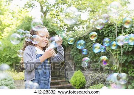 Stock Image - Girl blowing bubbles in backyard. Fotosearch