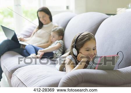 Stock Photo - Girl with headphones and digital tablet laying on living room sofa. Fotosearch