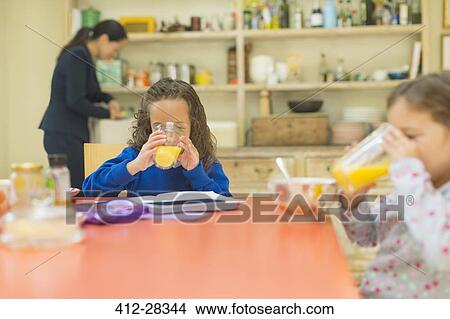 Picture - Girls drinking orange juice at breakfast table. Fotosearch