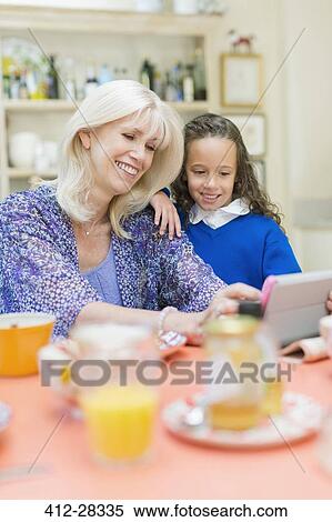 Stock Photography - Grandmother and granddaughter using digital tablet at breakfast table. Fotosearch