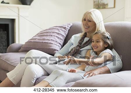 Stock Photography - Grandmother and granddaughter watching TV on living room sofa. Fotosearch