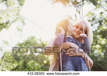 Stock Image - Grandmother hugging granddaughter on swing. Fotosearch