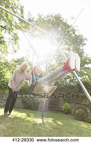 Stock Image - Grandmother pushing carefree granddaughter on swing in backyard. Fotosearch