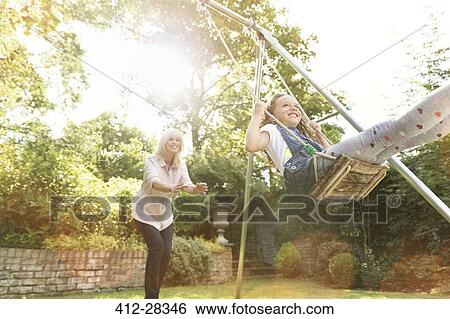 Grandmother pushing granddaughter on swing in backyard View Large Photo Image Stock Photograph - Grandmother pushing granddaughter on swing in backyard. Fotosearch