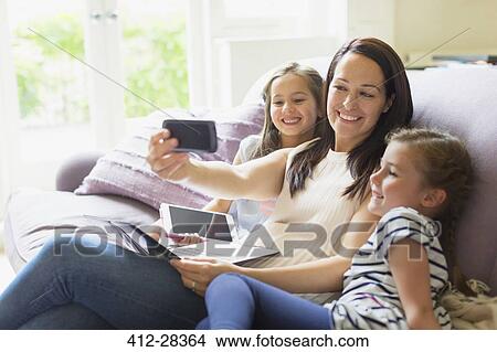 Mother and daughters taking selfie on living room sofa View Large Photo Image Picture - Mother and daughters taking selfie on living room sofa. Fotosearch