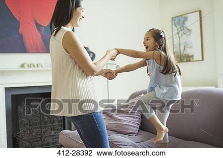 Stock Image - Playful mother and daughter dancing in living room. Fotosearch