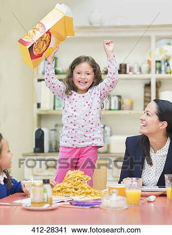 Stock Image - Portrait enthusiastic girl cheering with cereal box at breakfast table. Fotosearch